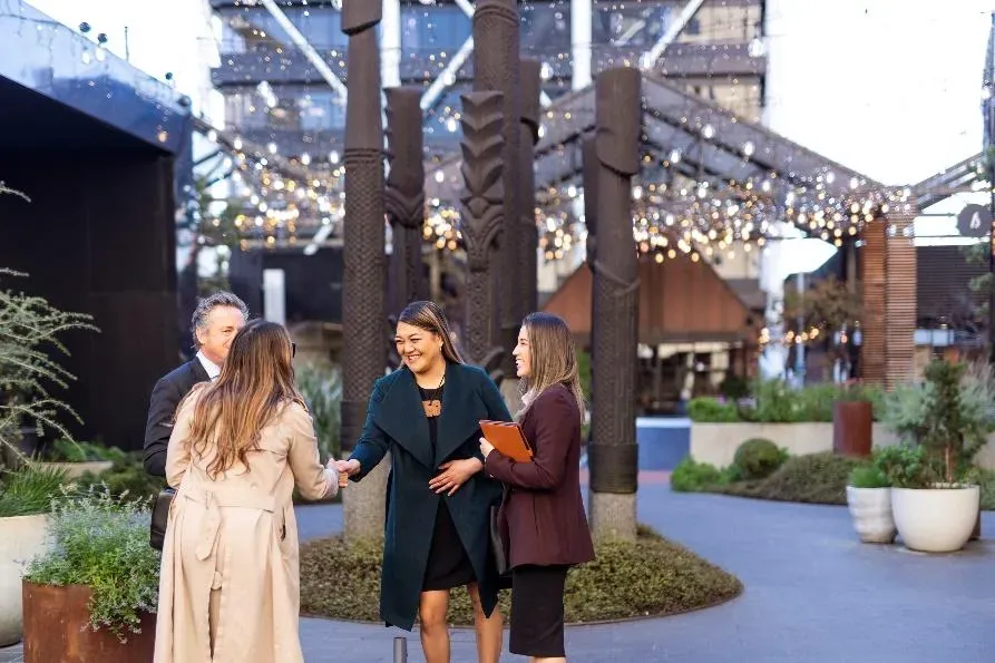People shaking hands in from of some carved Māori poles People shaking hands in from of some carved Māori poles