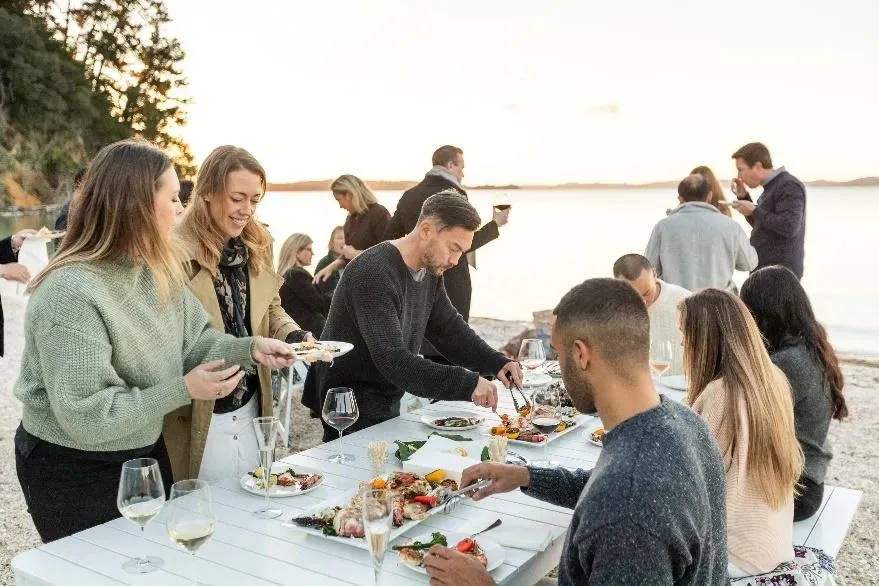 People sitting around a table near a beach enjoying a meal People sitting around a table near a beach enjoying a meal